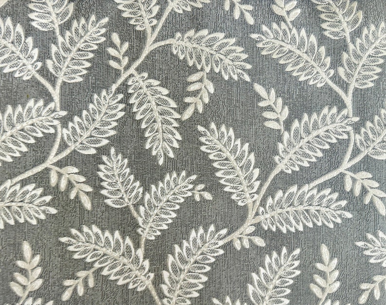 K&ouml;nnte beinhalten: Ein grauer Stoff mit einem wei&szlig;en floralen Muster aus Bl&auml;ttern und Zweigen. Der Stoff hat eine strukturierte Oberfl&auml;che.