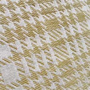 May include: A woven fabric featuring a repeating houndstooth pattern in shades of olive green and white. The textile displays a distinct diagonal texture created by the interlacing threads, showcasing a consistent geometric design throughout the surface.