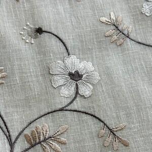 May include: White sheer fabric with embroidered brown vines and white flowers. The fabric has a subtle texture.