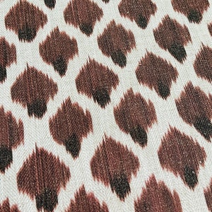 May include: Close-up of a white fabric with a brown and black ikat pattern. The pattern resembles a leopard print.