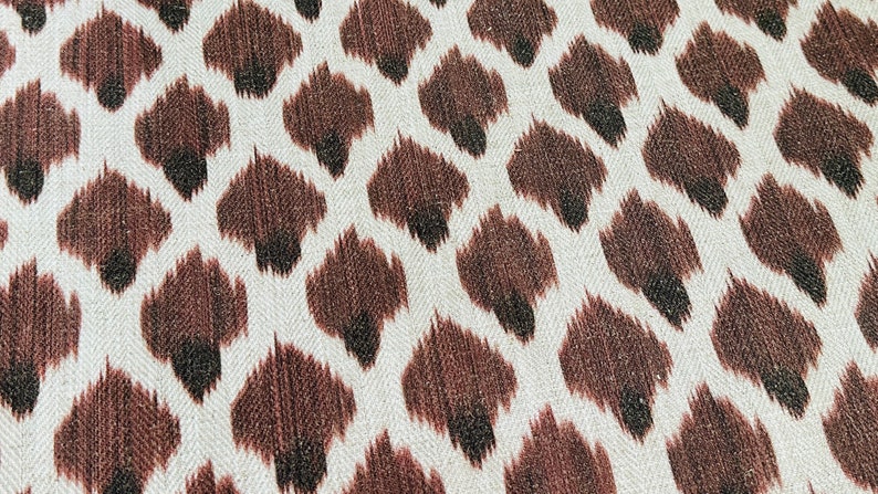 May include: Close-up of a white fabric with a brown and black ikat pattern. The pattern resembles a leopard print.