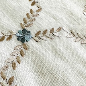 Puede incluir: Tela blanca con un delicado patr&oacute;n bordado de hojas marrones y flores azul verdoso. La tela tiene una textura sutil.