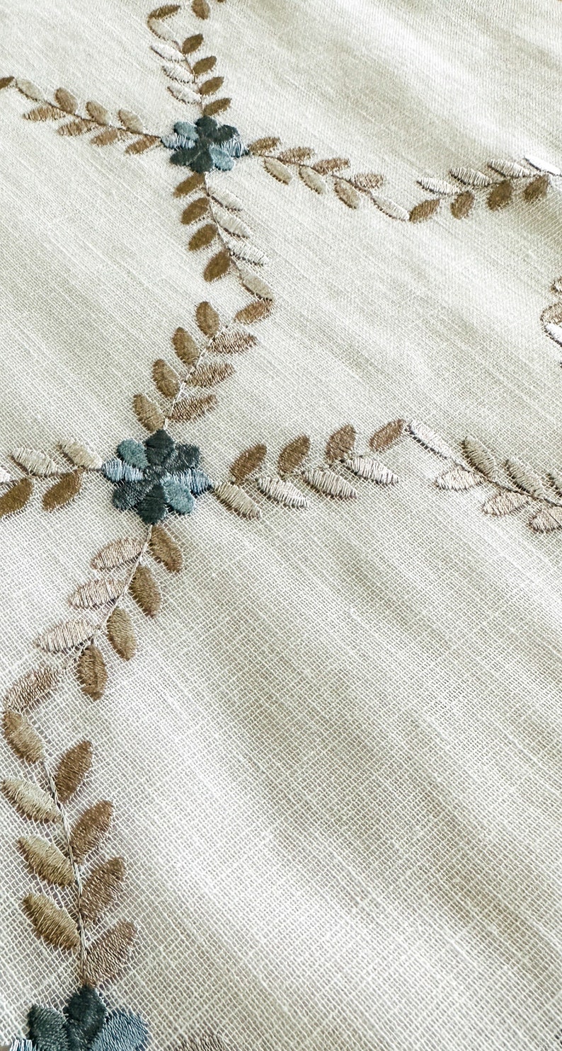Puede incluir: Tela blanca con un delicado patr&oacute;n bordado de hojas marrones y flores azul verdoso. La tela tiene una textura sutil.