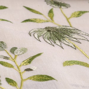 May include: White fabric with green embroidered floral designs. The flowers are stylized and have a delicate, almost translucent appearance.
