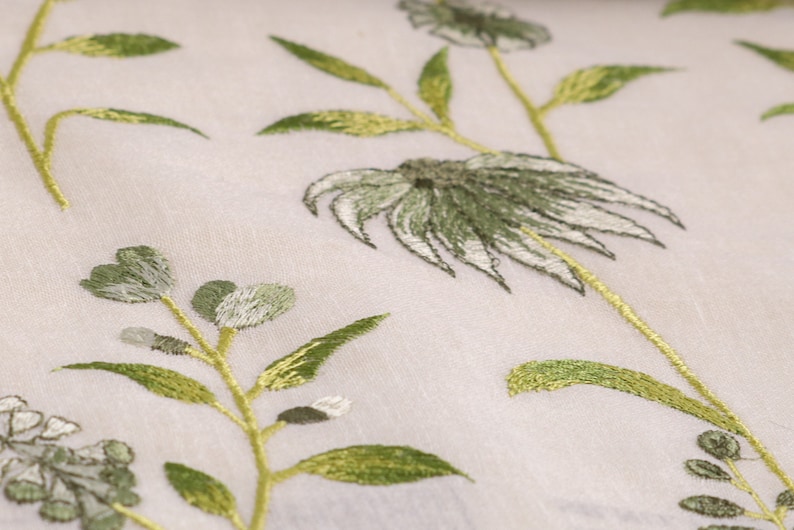 May include: White fabric with green embroidered floral designs. The flowers are stylized and have a delicate, almost translucent appearance.