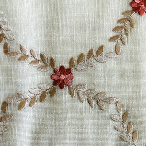 Puede incluir: Un mantel de mesa de tela blanca con un dise&ntilde;o floral bordado en marr&oacute;n. Las flores son rojas y las hojas son marrones.
