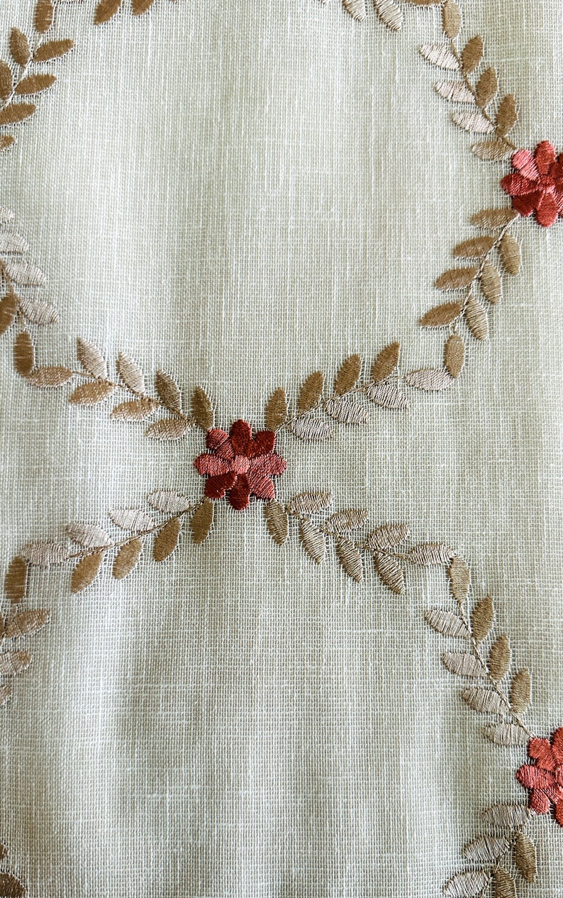 Puede incluir: Un mantel de mesa de tela blanca con un dise&ntilde;o floral bordado en marr&oacute;n. Las flores son rojas y las hojas son marrones.