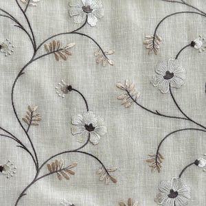 May include: A beige fabric with an embroidered floral pattern in shades of brown and white. The flowers are stylised and have a delicate, vintage look.