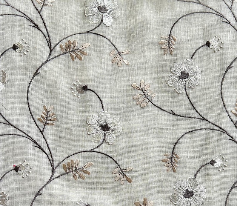 May include: A beige fabric with an embroidered floral pattern in shades of brown and white. The flowers are stylised and have a delicate, vintage look.