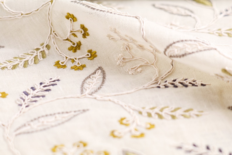 May include: White fabric with embroidered floral designs in shades of green, brown, and white.