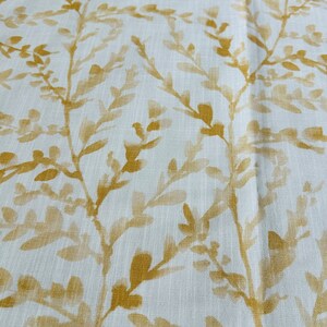May include: White fabric with a subtle texture featuring a repeating pattern of gold-colored leafy branches.