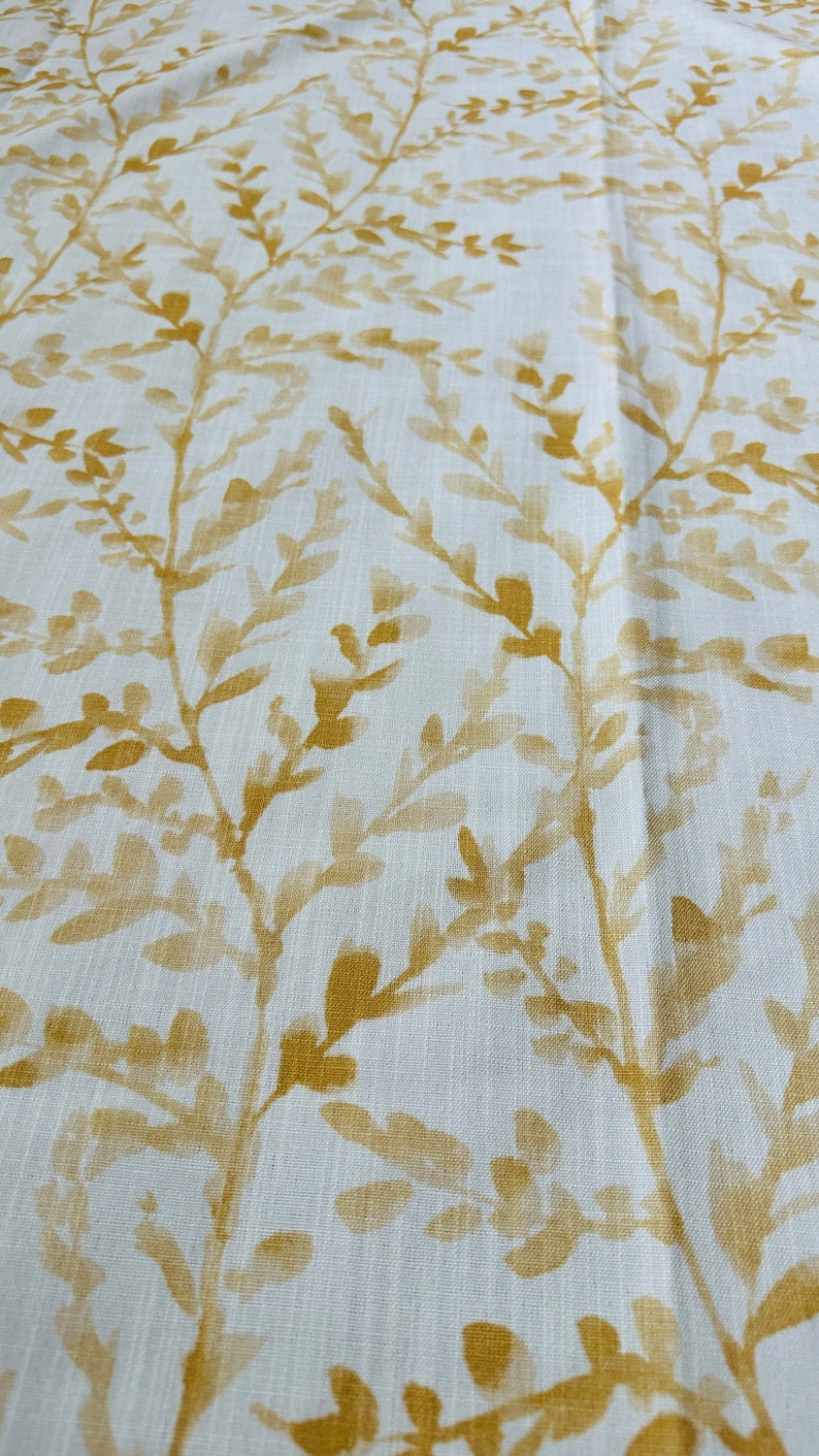 May include: White fabric with a subtle texture featuring a repeating pattern of gold-colored leafy branches.