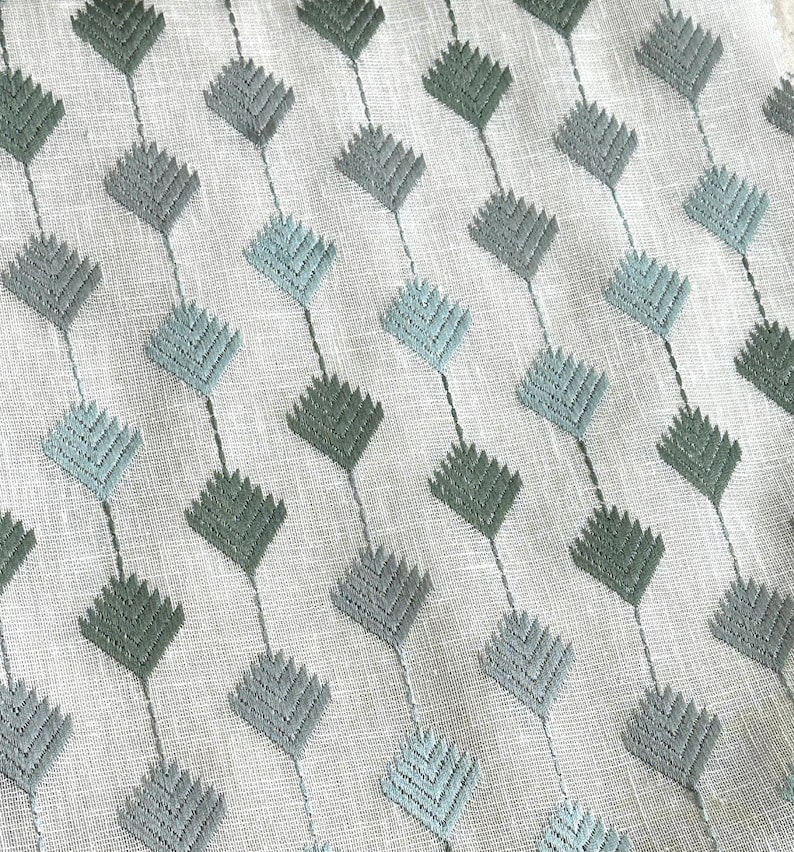 May include: A white fabric with a repeating pattern of light blue and dark green diamond shapes. The fabric has a subtle texture.