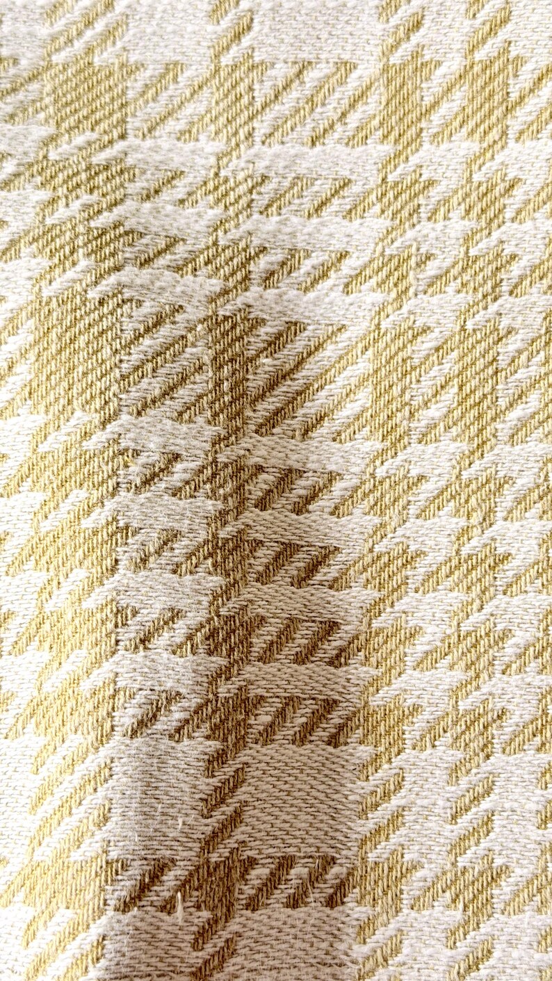 May include: A woven fabric featuring a repeating houndstooth pattern in shades of golden yellow and off-white. The textile displays a textured surface with visible interlaced threads, creating a consistent geometric design across the entire material.
