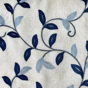 May include: A white fabric with a blue and gray embroidered floral pattern. The pattern features leaves and vines.