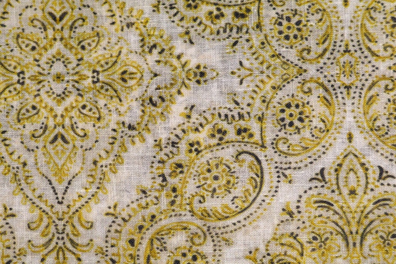 May include: A white fabric with a paisley pattern in shades of gold and black.