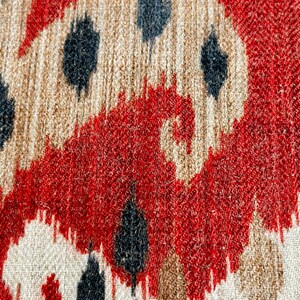 May include: Close-up of a fabric with a red, white and black ikat pattern. The fabric has a textured surface and a woven appearance.