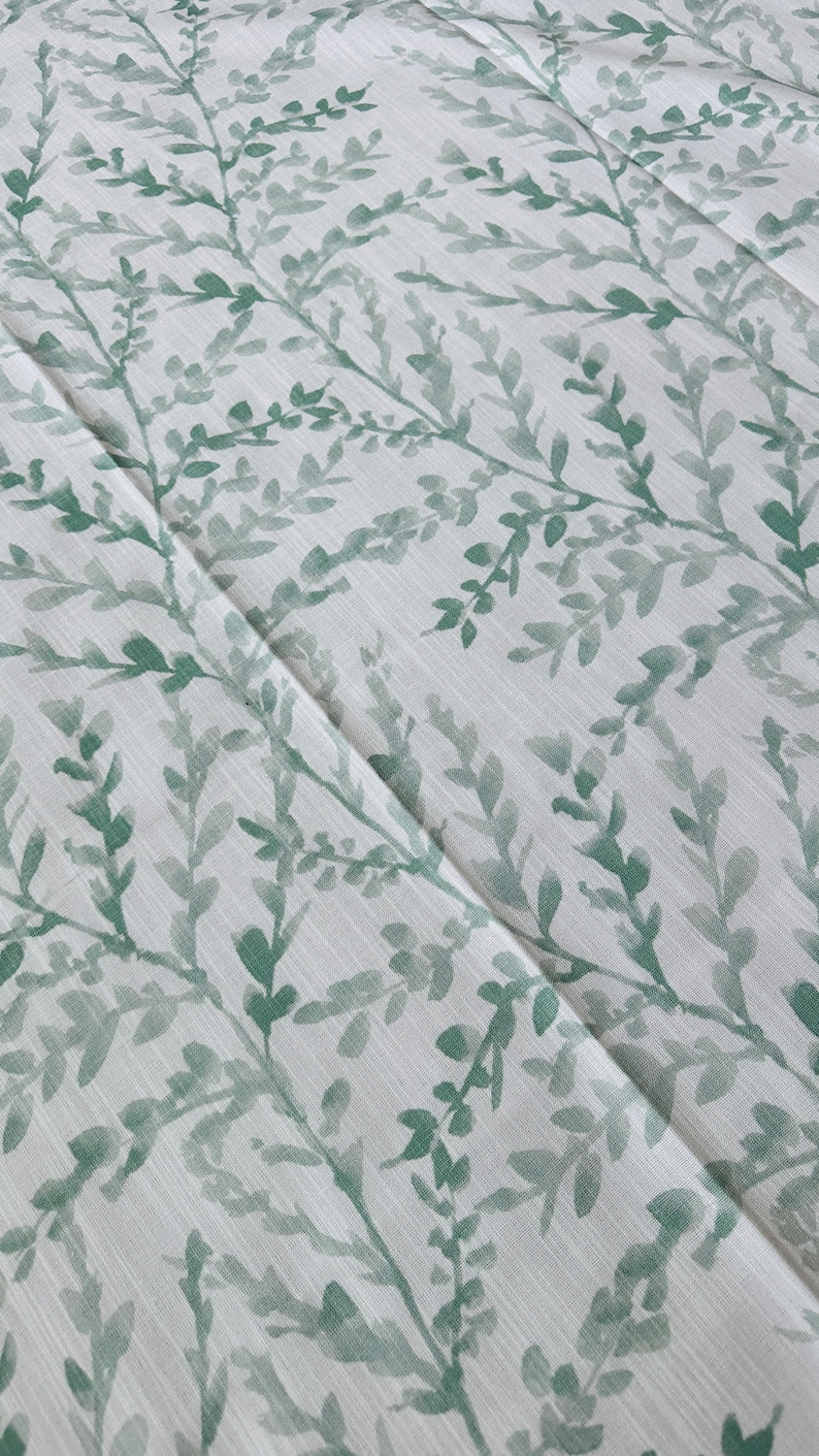 May include: White fabric with a green leafy pattern. The leaves are a watercolor style and are scattered across the fabric.