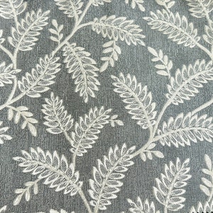 K&ouml;nnte beinhalten: Nahaufnahme eines grauen Stoffes mit einem wei&szlig;en Blumenmuster. Das Muster besteht aus kleinen Bl&auml;ttern und Zweigen.