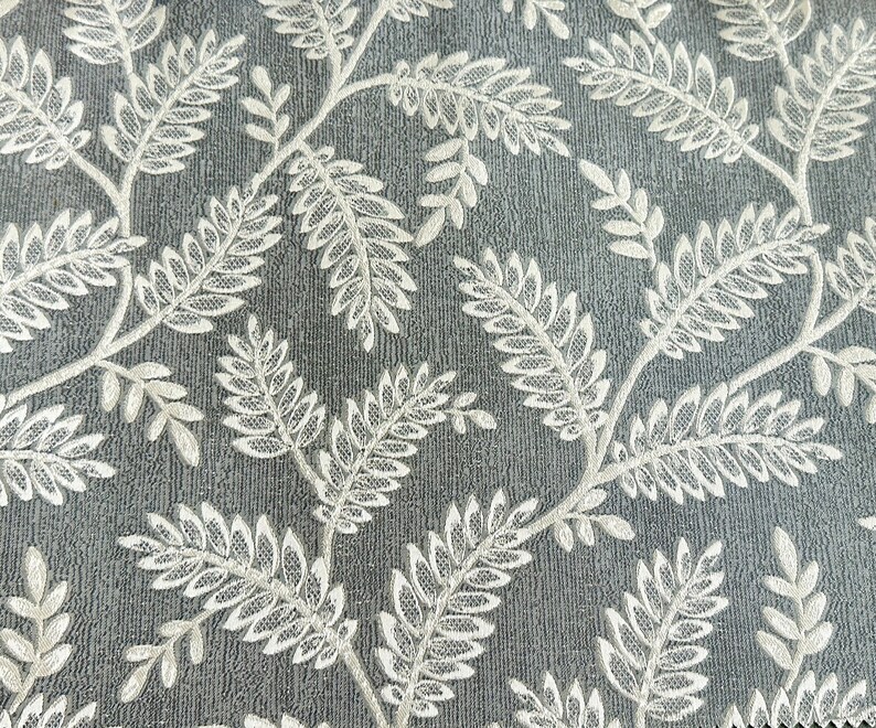 K&ouml;nnte beinhalten: Nahaufnahme eines grauen Stoffes mit einem wei&szlig;en Blumenmuster. Das Muster besteht aus kleinen Bl&auml;ttern und Zweigen.