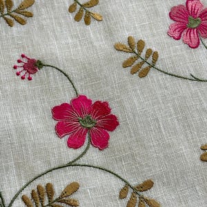 May include: White fabric with embroidered pink flowers and gold leaves. The flowers have a green center.