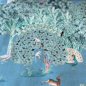 May include: A blue fabric with a repeating pattern of a jungle scene. The pattern includes peacocks, monkeys, deer, and birds. The background is a light blue colour.