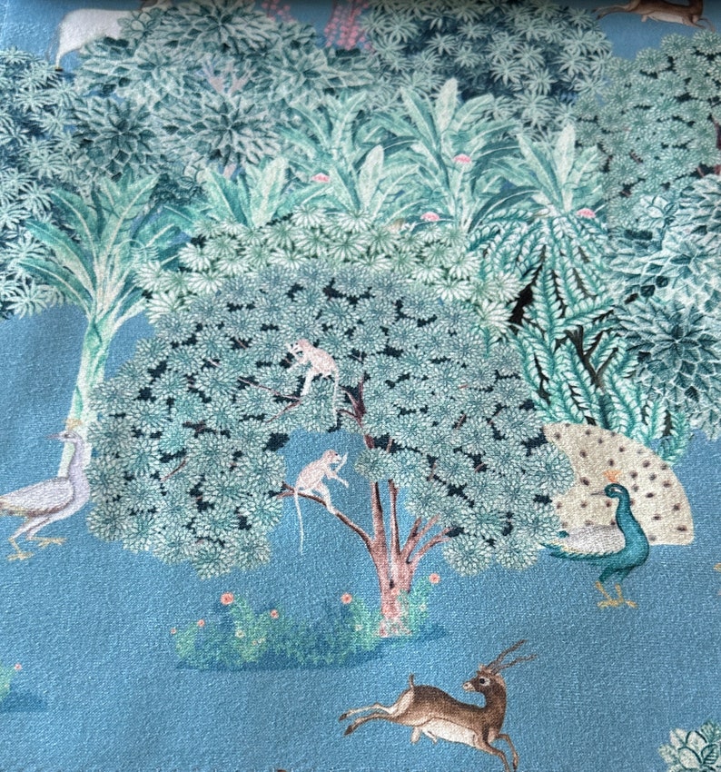 May include: A blue fabric with a repeating pattern of a jungle scene. The pattern includes peacocks, monkeys, deer, and birds. The background is a light blue colour.