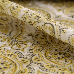 May include: A close-up of a white fabric with a yellow and black paisley pattern. The fabric is folded in half, and the pattern is visible on both sides.