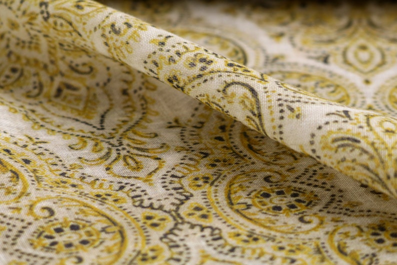 May include: A close-up of a white fabric with a yellow and black paisley pattern. The fabric is folded in half, and the pattern is visible on both sides.