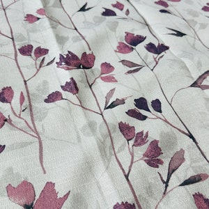 May include: A white fabric with a subtle texture features a repeating pattern of dark purple stylized floral sprigs. The fabric has a soft, slightly wrinkled appearance.
