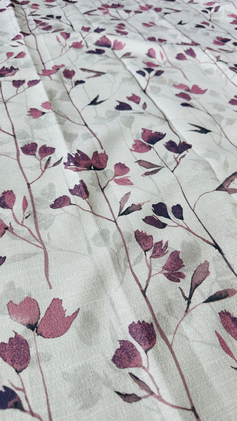 May include: A white fabric with a subtle texture features a repeating pattern of dark purple stylized floral sprigs. The fabric has a soft, slightly wrinkled appearance.