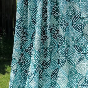 May include: A white fabric curtain with a teal and green geometric pattern. The pattern is made up of repeating circles and diamonds.