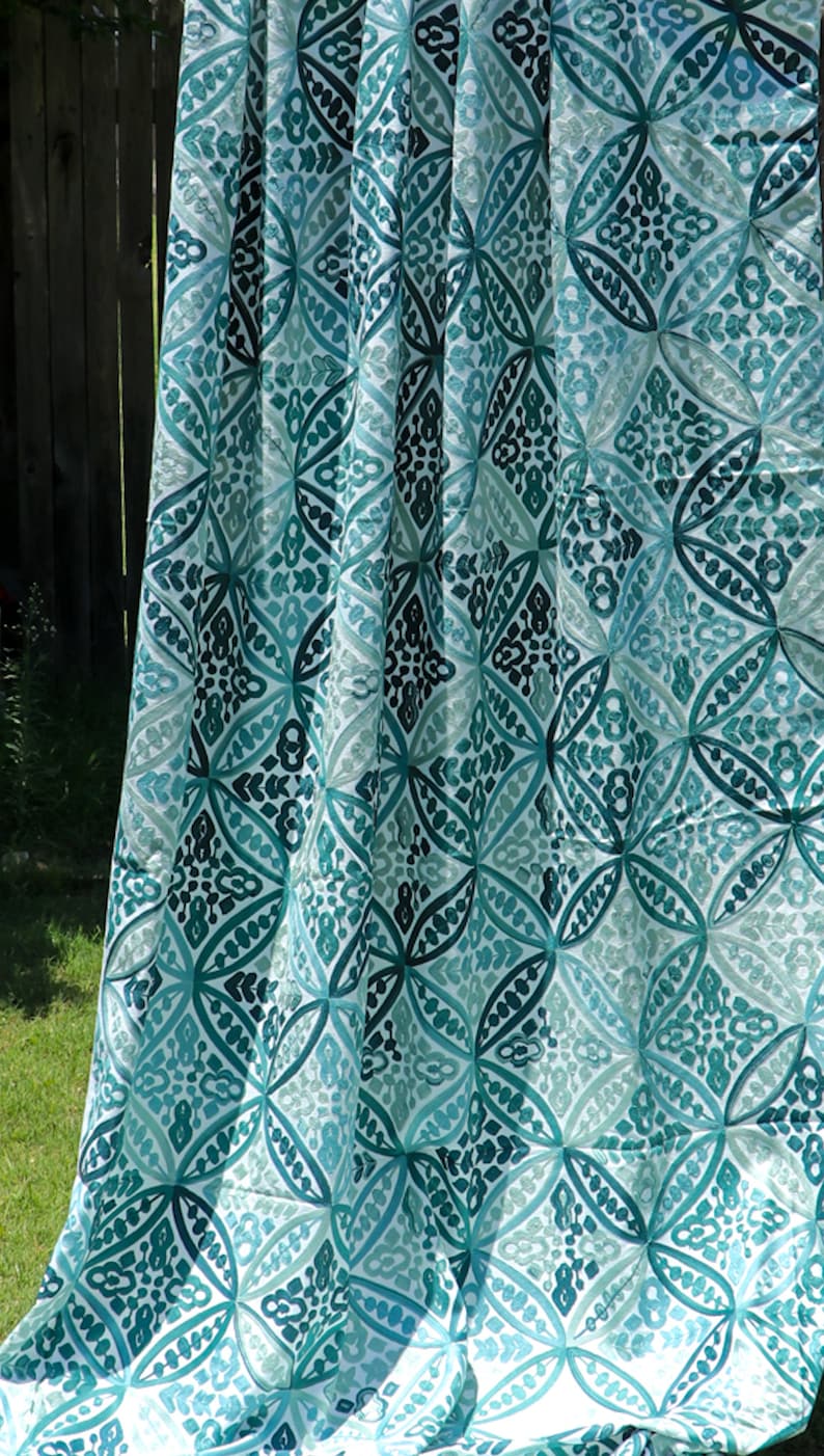 May include: A white fabric curtain with a teal and green geometric pattern. The pattern is made up of repeating circles and diamonds.