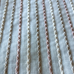 Puede incluir: Tela blanca con rayas tejidas de color rosa y beige. La tela tiene una textura sutil y una apariencia ligeramente transparente.