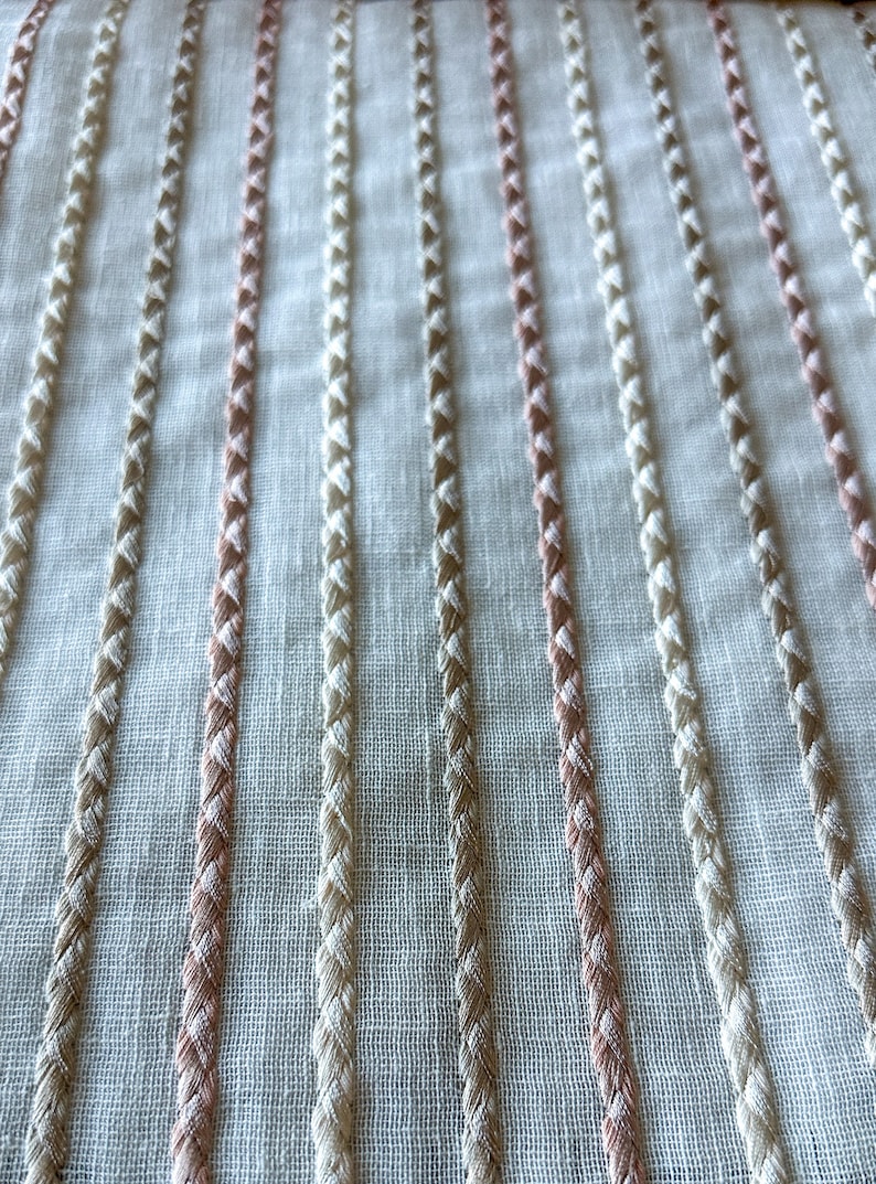 Puede incluir: Tela blanca con rayas tejidas de color rosa y beige. La tela tiene una textura sutil y una apariencia ligeramente transparente.