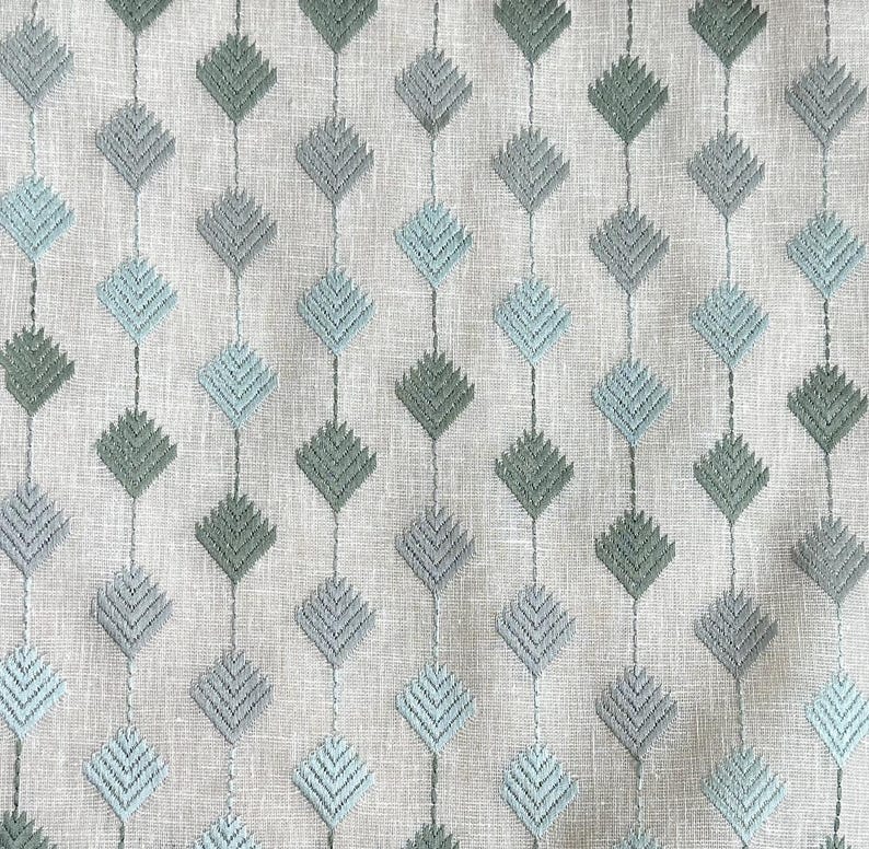 May include: A close-up of a fabric with a repeating pattern of light blue and green diamond shapes. The fabric has a subtle texture and a light gray background.