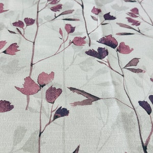 May include: A white fabric with a subtle, repeating pattern of purple flowers and leaves. The fabric has a slightly textured surface.
