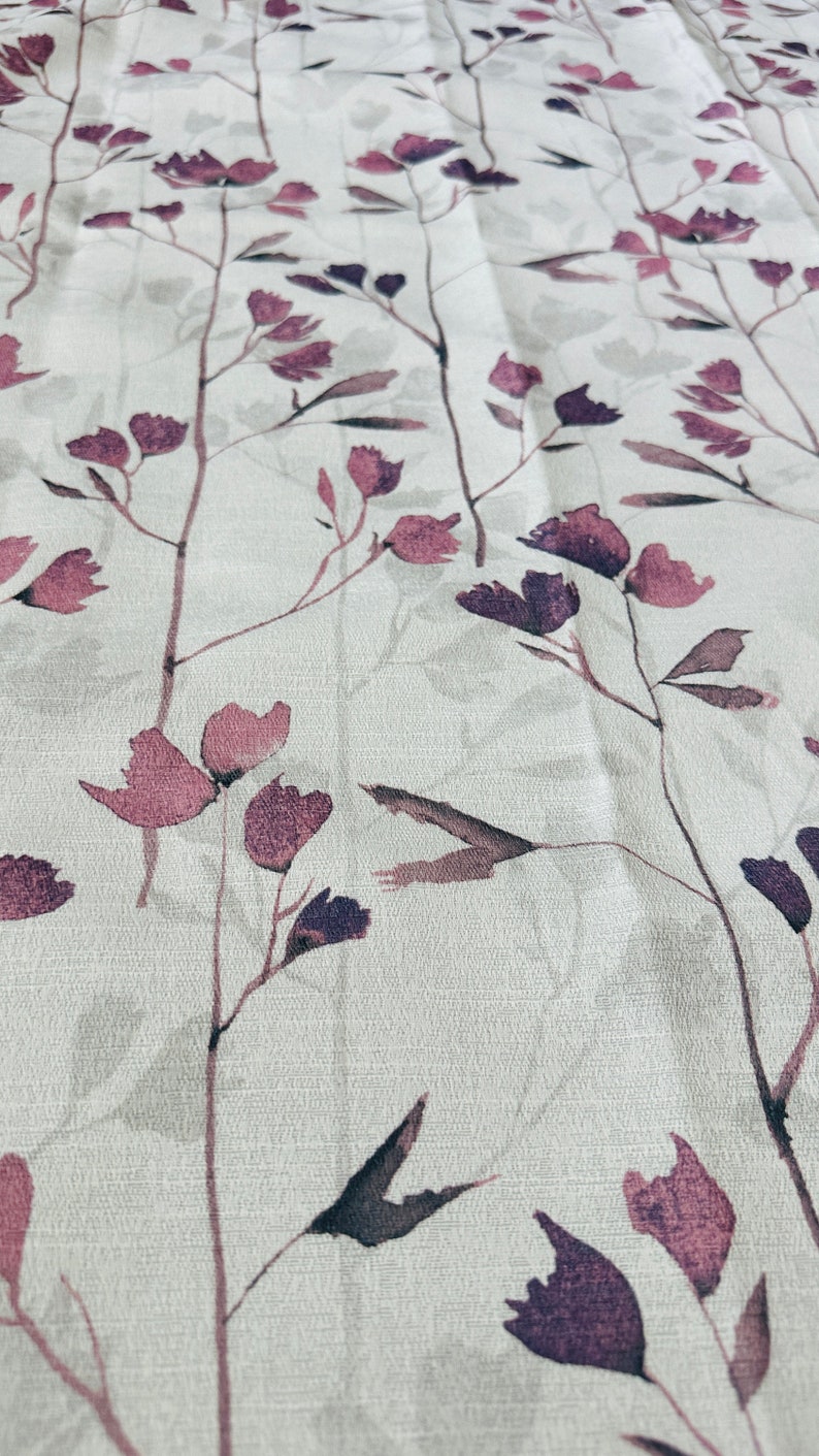 May include: A white fabric with a subtle, repeating pattern of purple flowers and leaves. The fabric has a slightly textured surface.