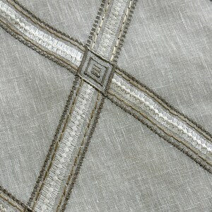 May include: A close-up of a light gray fabric with a pattern of white and brown embroidered lines forming a grid.
