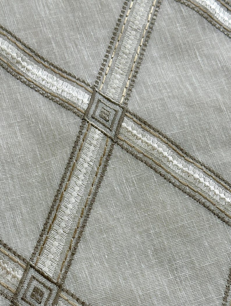 May include: A close-up of a light gray fabric with a pattern of white and brown embroidered lines forming a grid.