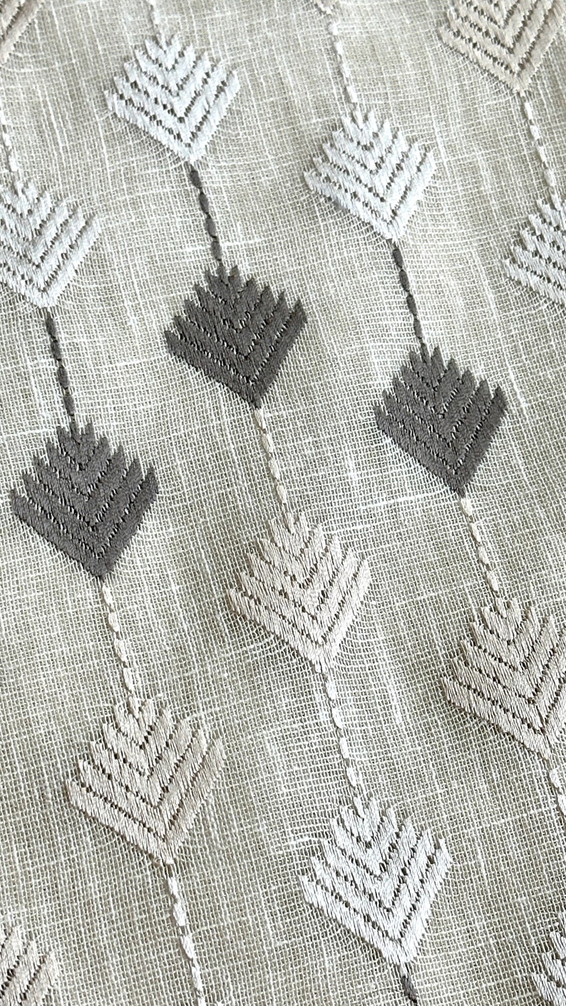 May include: Close-up of a light beige fabric with an embroidered pattern. The pattern features alternating gray and off-white leaf-like shapes connected by thin, vertical lines. The fabric has a textured appearance.