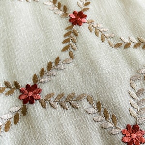 Puede incluir: Tela beige con hojas marrones y flores rojas bordadas. La tela tiene una textura sutil.