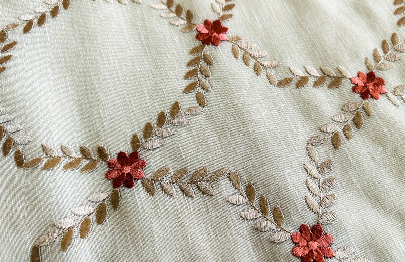 Puede incluir: Tela beige con hojas marrones y flores rojas bordadas. La tela tiene una textura sutil.
