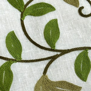 May include: Embroidered green leaves on a white linen fabric. The leaves are stitched in a detailed pattern, creating a delicate and elegant design.