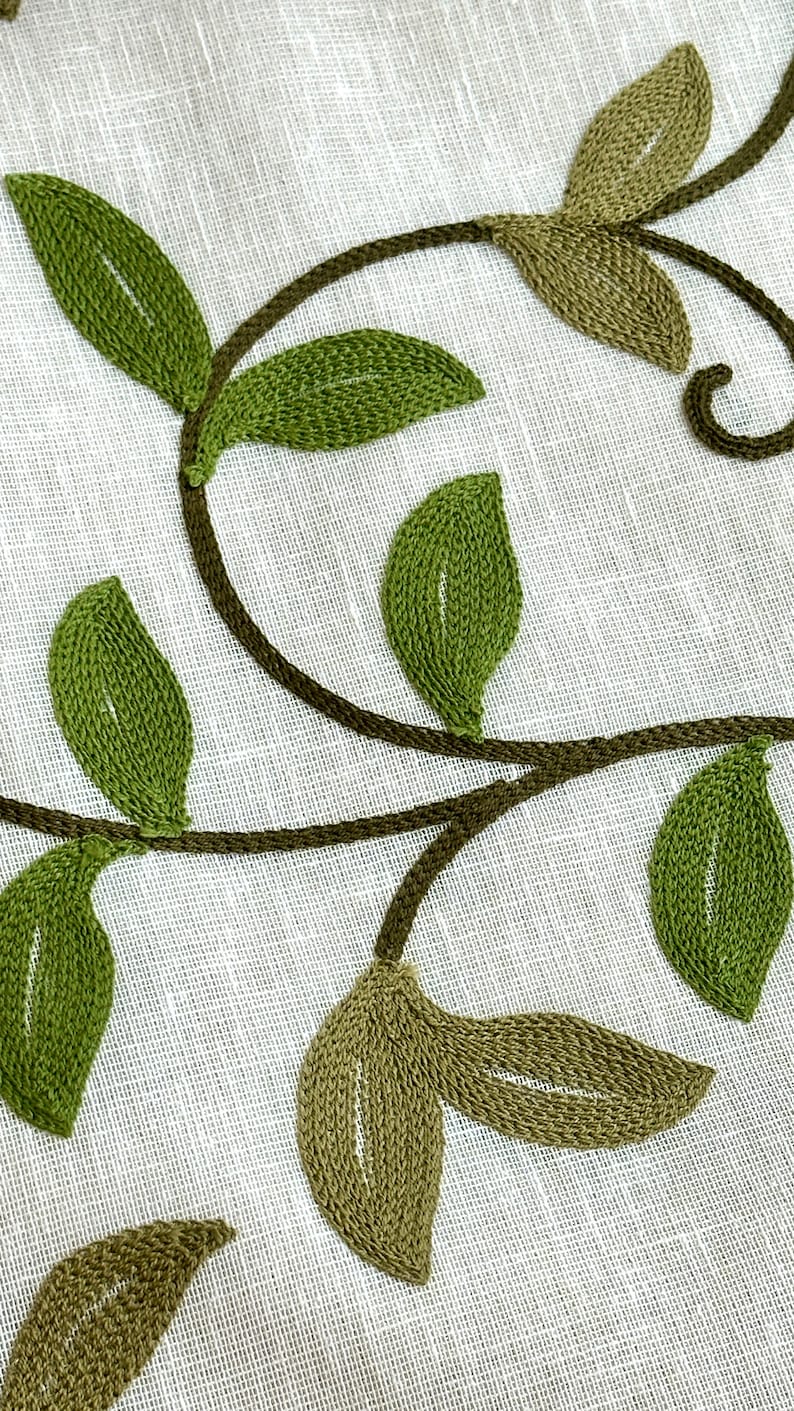May include: Embroidered green leaves on a white linen fabric. The leaves are stitched in a detailed pattern, creating a delicate and elegant design.