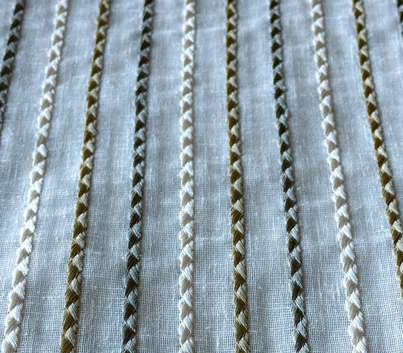 May include: White fabric with vertical stripes of different colored embroidery. The stripes are made of a braided stitch in white, gray, and brown.