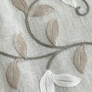 May include: Beige fabric with embroidered floral design featuring leaves and flowers in shades of white and brown.