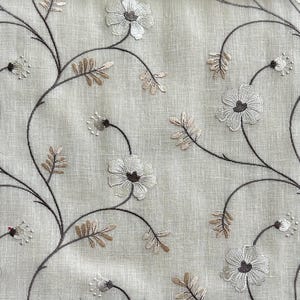 May include: A close-up of a beige fabric with embroidered floral designs in shades of brown and white.