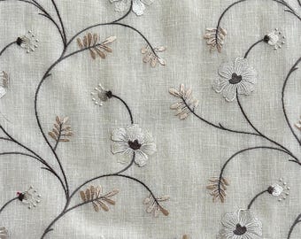 May include: A close-up of a beige fabric with embroidered floral designs in shades of brown and white.
