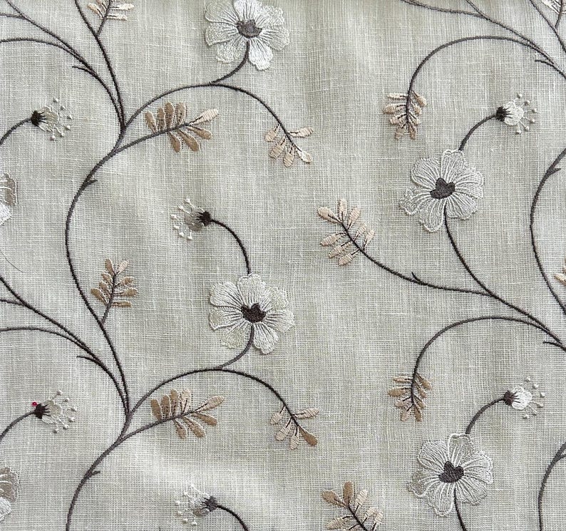 May include: A close-up of a beige fabric with embroidered floral designs in shades of brown and white.